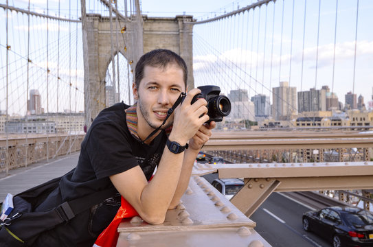 USA, New York, portrait of traveler with camera standing on Brooklyn Bridge in the evening