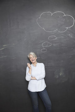 Happy mature teacher standing at blackboard with thought bubble