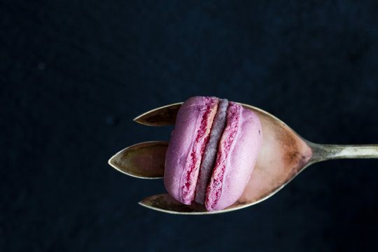 Pink macaron on silver spoon in front of black background
