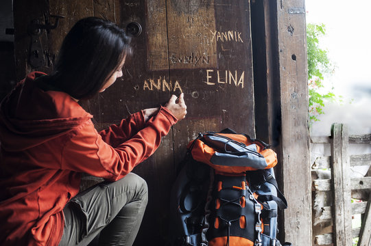 Austria, Altenmarkt-Zauchensee, young female hiker carving her name in wooden door of Alpine Cabin