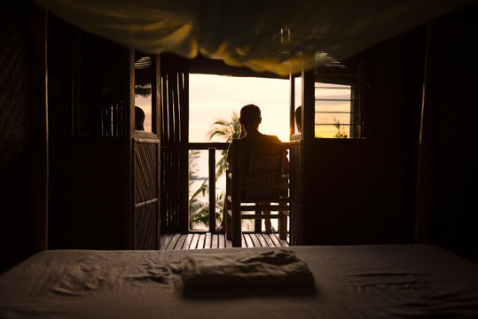 Philippines, Apo Island, man on the terrace of a wooden hut enjoying sunset
