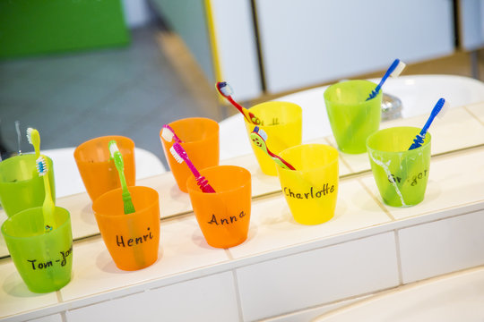 Plastic cups with toothbrushes with manes of kids in nursery