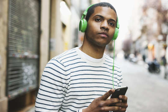 Spain, Barcelona, portrait of young man hearing music with green headphones on street