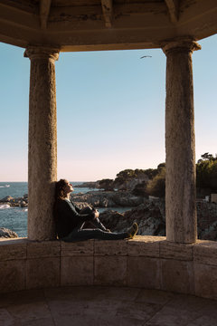 Spain, Costa Brava, Sant Feliu de Guixols, woman resting in an arbor by the sea at sunset