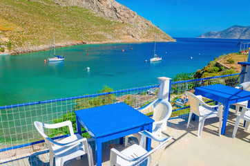 Fototapeta na wymiar Blue wooden tables and chairs in bay, Greek Island