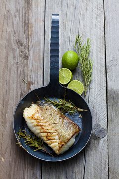 Cast-iron frying pan with piece of fried Norwegian codfish and twigs of rosemary