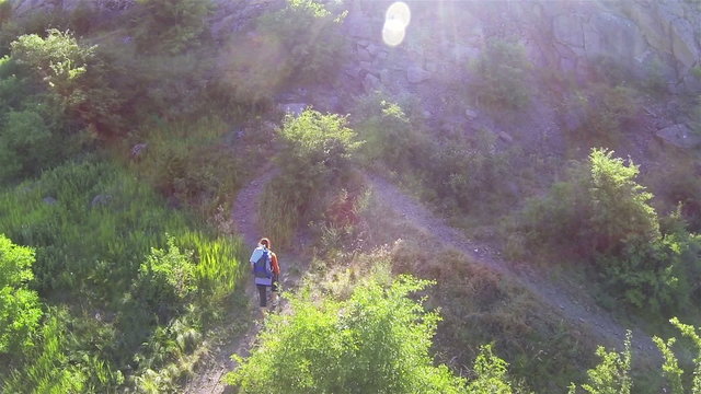 
Slender girl with tracking sticks goes up  mountain track. Aerial
