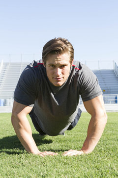 USA, California, San Luis Obispo, portrait of young man doing pushups on an athletic field