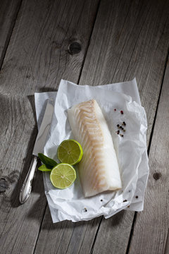 Filet of codfish, lime and knife, and peppercorns on greaseproof paper on wood
