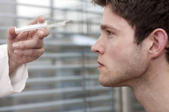 Doctor holding syringe at face of young man