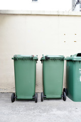 Green plastic garbage bin on white wall in factory