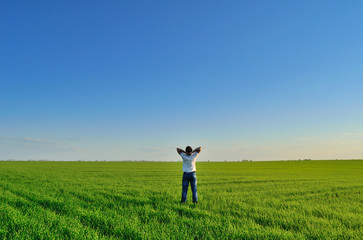 Naklejka na ściany i meble Young man on the summer green field under clear skies