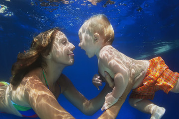 Portrait of child swimming underwater with fun in pool with diving positive mother. Healthy...