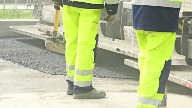 Road construction worker leveling asphalt using rake on the new road 
