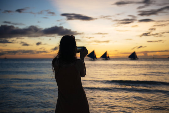 Woman photographing sailboats at sunset, Philippines
