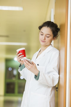 Young doctor with cell phone and coffee cup on hospital floor