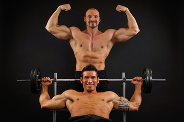 Fototapeta na wymiar Two muscular man posing with dumbells on dark background