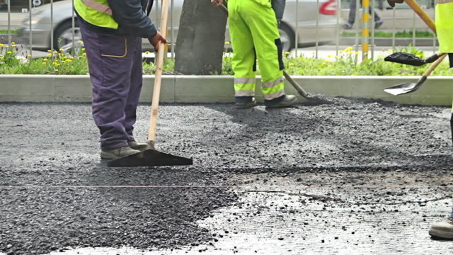 Road construction worker leveling asphalt using rake on the new road 