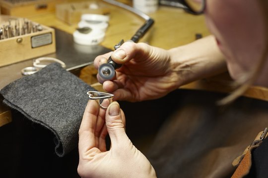 Goldsmith in workshop working on heart-shaped piece of jewelry
