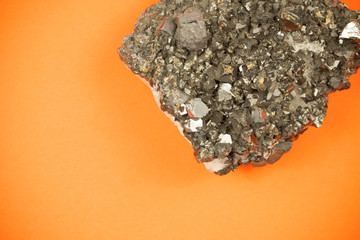 Picture of a cut block of black lead ore with irregular texture, shot on orange paper background with soft shadows, symbolizing playful approach to mining and natural resources industries