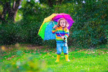 Little girl playing in the rain holding colorful umbrella