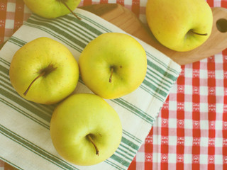 Apples on cutting board with green and white table napkin and on checkered red and white table cloth