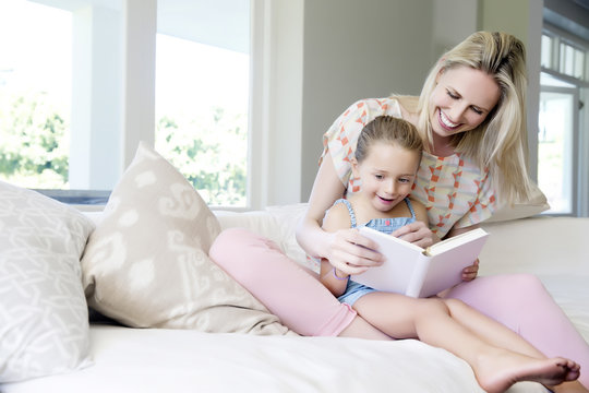 Mother and daughter sitting on sofa, reading book