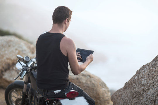 South Africa, Cape Town, motorcyclist at the coast taking pictures with digital tablet