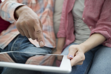 The couple are relaxing on the sofa while watching the tablet