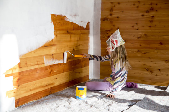 Girl painting wooden wall with paint roller