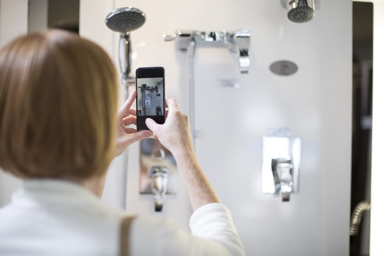 Woman taking pictures with her smartphone of taps in a bathroom shop