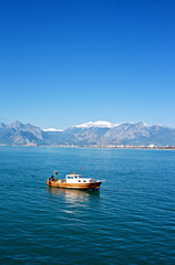 Small fishing boat with snow covered mountains in Antalya Turkey