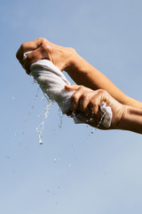 Hands squeeze wet fabric against blue sky.