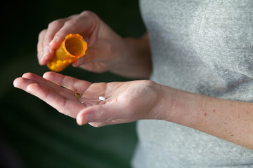 Close up of a woman's hands holding a pill bottle in one hand and a pill in the other.