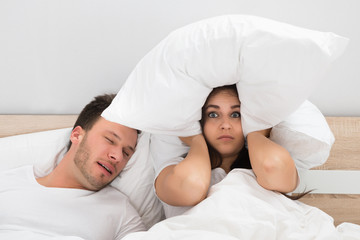 Woman Covering Ears While Man Snoring On Bed At Home