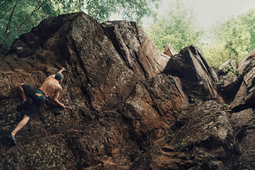 Sporty young man climbing on stone rock