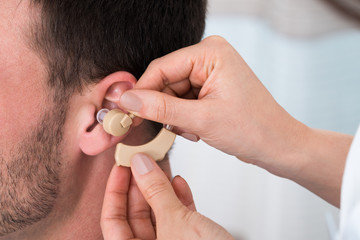 Hands Inserting A Hearing Aid Into A Man's Ear