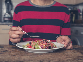 Young man eating salad in kitchen