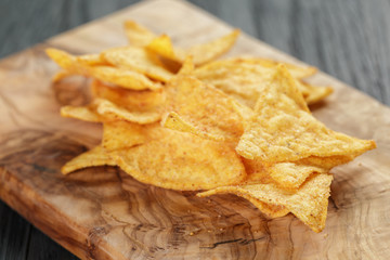 heap of tortilla chips on olive board on wooden table