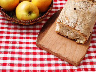 Picnic stil life with bread on wooden cutting board and apples in a basket on red checkered table cloth