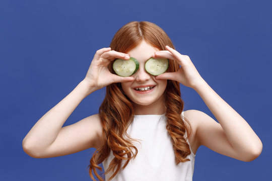 Smiling little girl holding slices of cucumber 