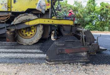 Worker operating industrial asphalt paver machine during highway construction and repairing works