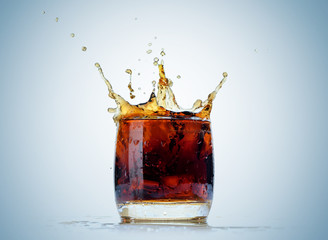 Ice cube droped in cola glass and cola splashing