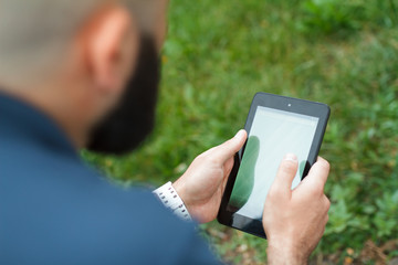 Bearded bald man sitting on a bench and read tablet at the alley