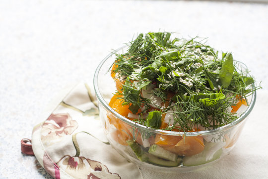 Salad of fresh yellow tomatoes and cucumber with herbs and sesame seeds in a glass bowl on a table