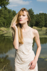 Fototapeta na wymiar Girl in white dress outdoor, posing on lake shore