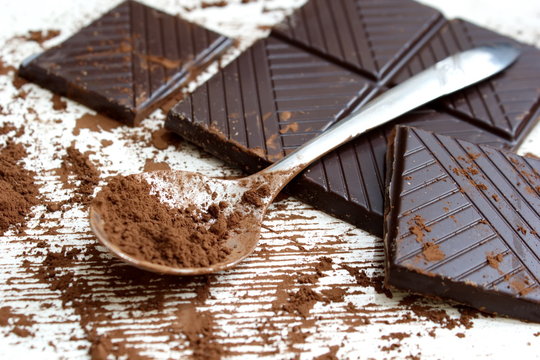 Chocolate Powder On A Spoon And Pieces Of Dark Chocolate On White Background