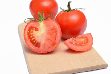 Pomodori rossi su un tagliere tagliati a meta e a spicchi, uno intero su sfondo bianco