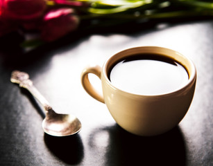 cup of coffee with tulip and book on black background