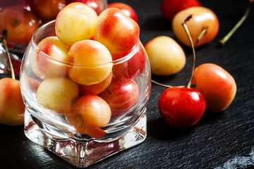 Red and yellow ripe cherries in a glass bowl, selective focus